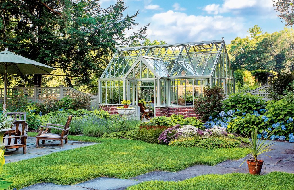 Garden with a green-framed glasshouse and mixed perennial borders