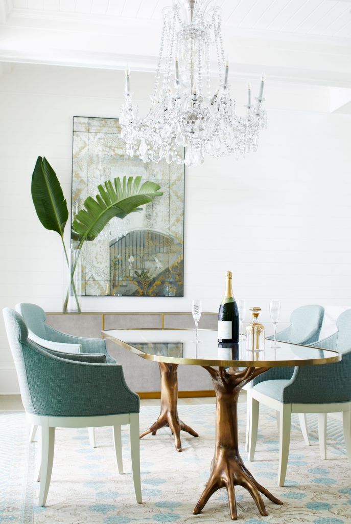 Breakfast area with teal chairs, a brass-based table and a chandelier