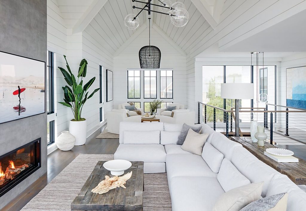 Home builder Marnie Oursler collaborated with her clients to create a dream beach home that combined traditional and contemporary aspects. In the great room, chic white furnishings keep the open space clean, crisp, and comfortable against the stunning seaside views.