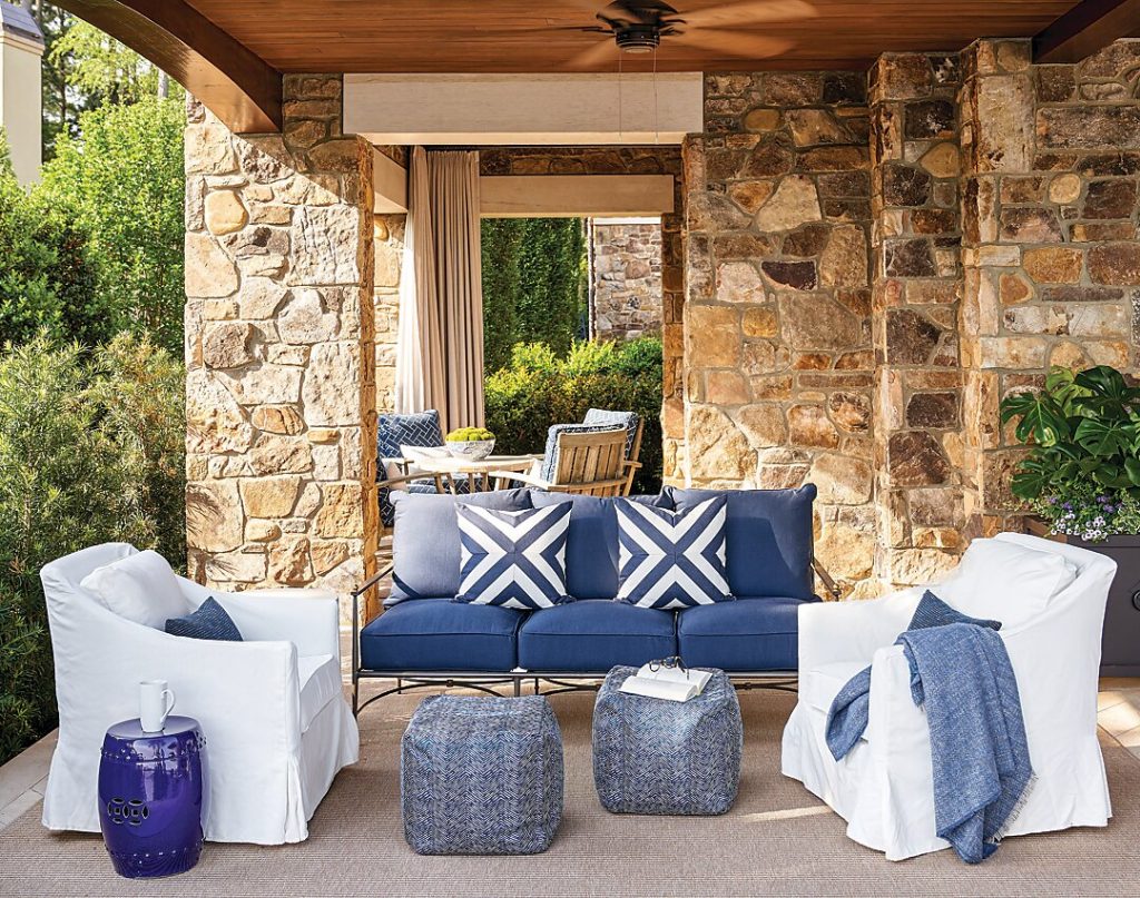 Stone loggia with a white sofa, navy pillows and woven stools