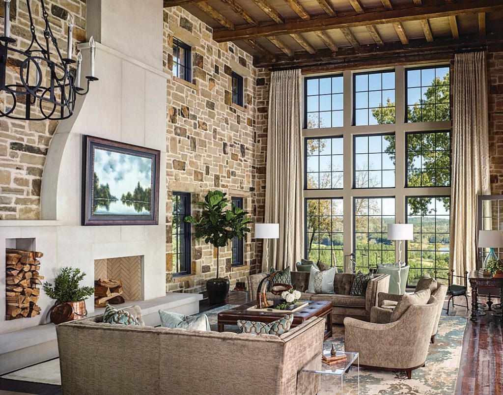 Two-story stone living room with steel windows and stacked firewood