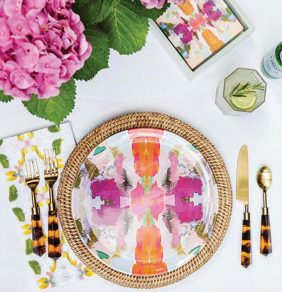 Place setting with a pink abstract plate, rattan charger and tortoise flatware