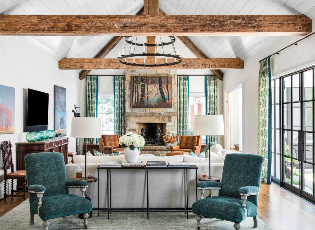 Great room with exposed beams, teal chairs and a stone fireplace