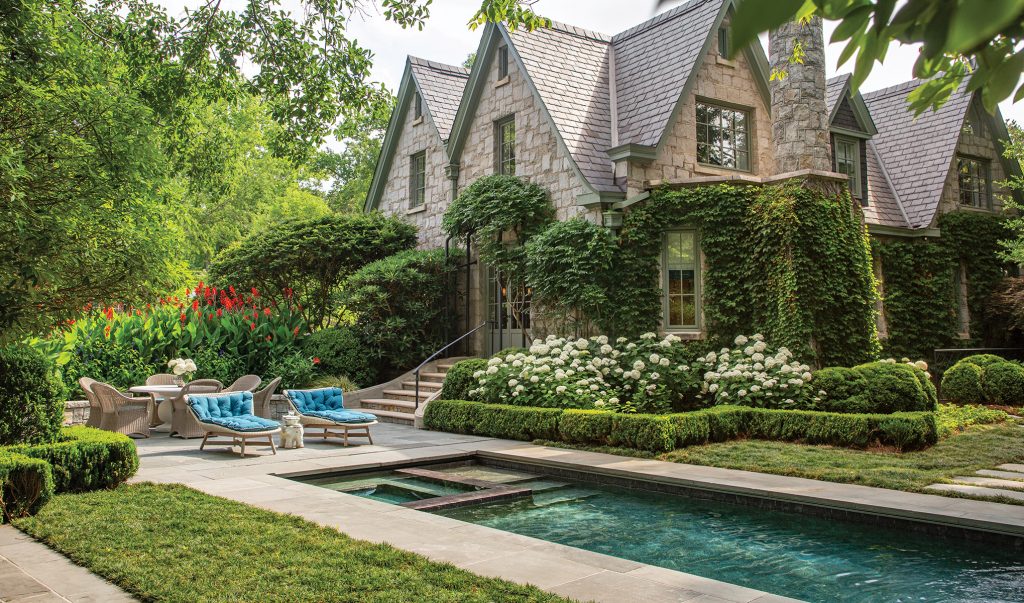 Ivy-covered stone house above a rectangular pool and clipped hedges