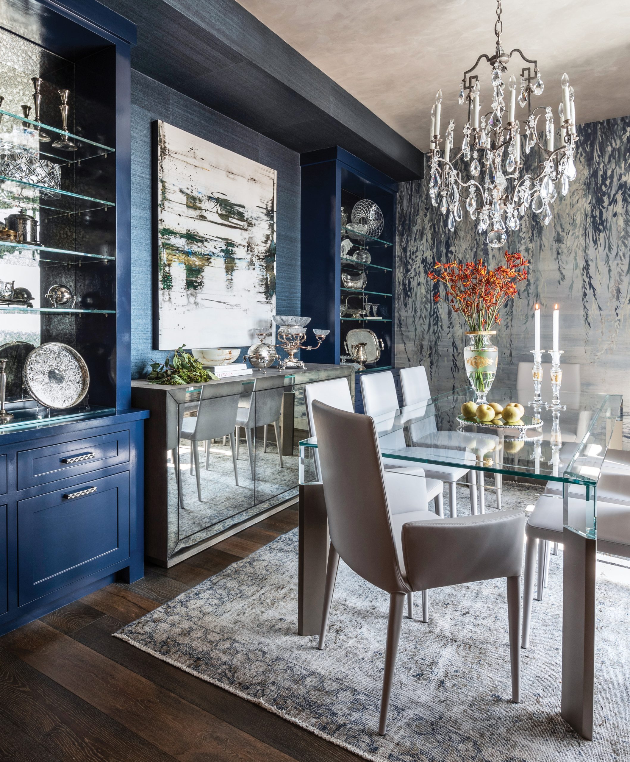 Navy dining room with a mirrored wall, chandelier and glass table