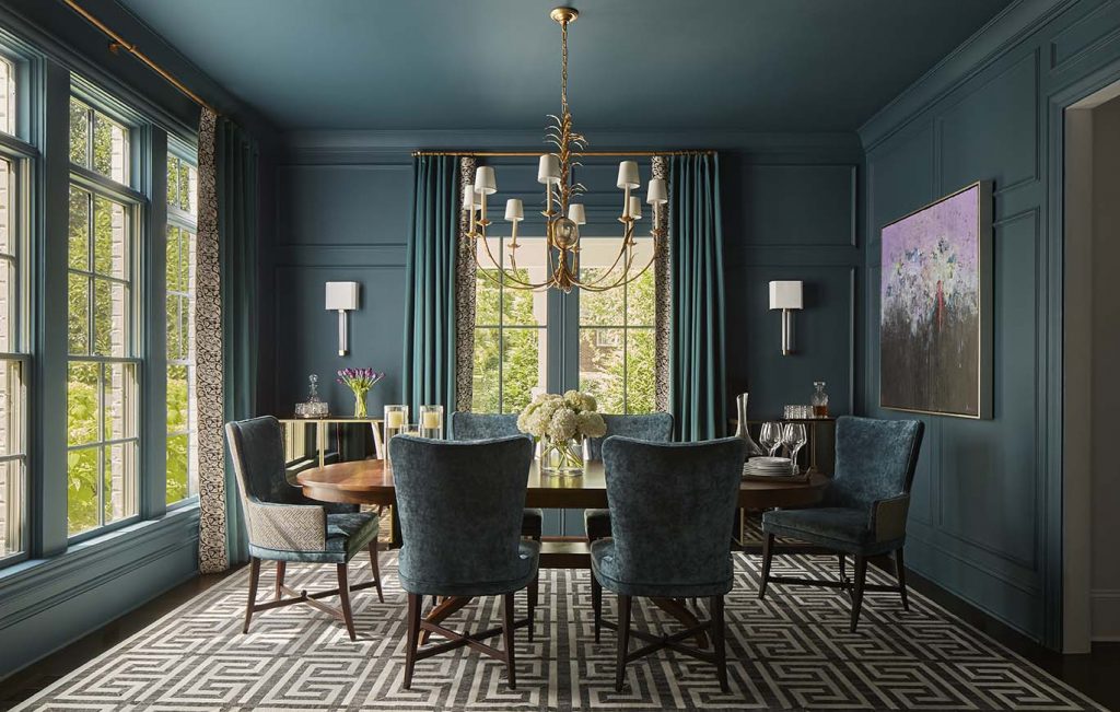 Teal dining room with a chandelier, dark chairs and a graphic rug