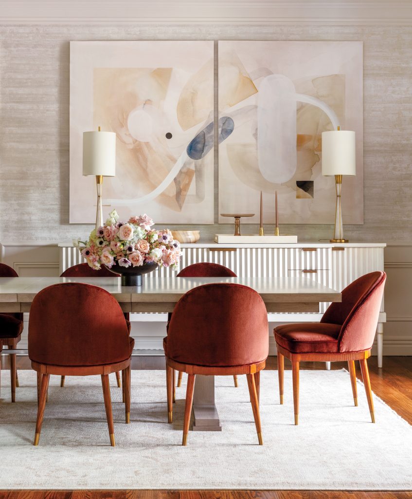 Dining table with rust velvet chairs below paired abstract canvases