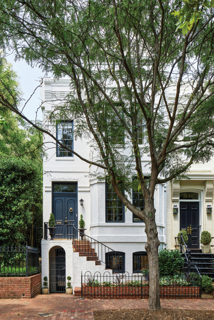 Narrow townhouse with a stoop and iron rail beneath a bare tree