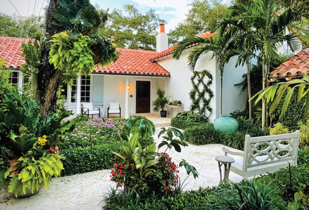 White stucco house with a red tile roof behind lush tropical planting