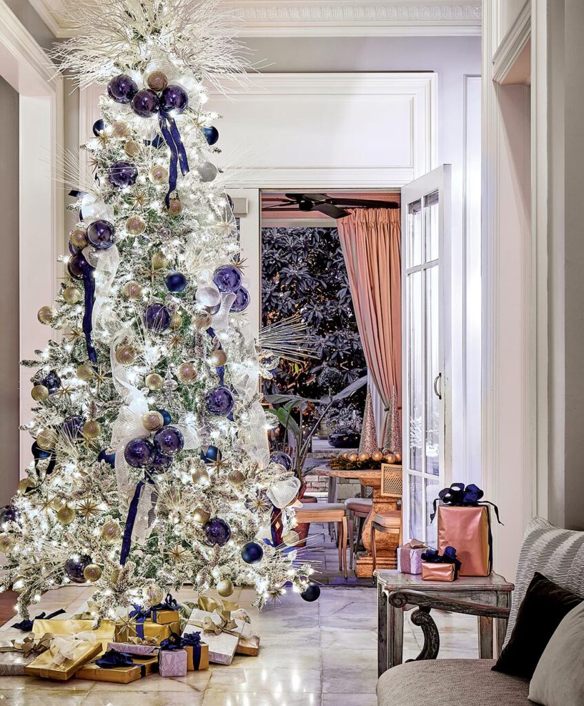Flocked Christmas tree trimmed with purple ribbon in a tall hall