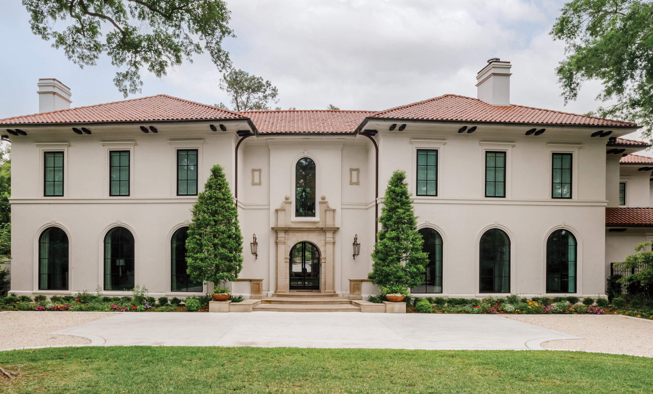 Stucco house with arched windows and a tile roof across a lawn
