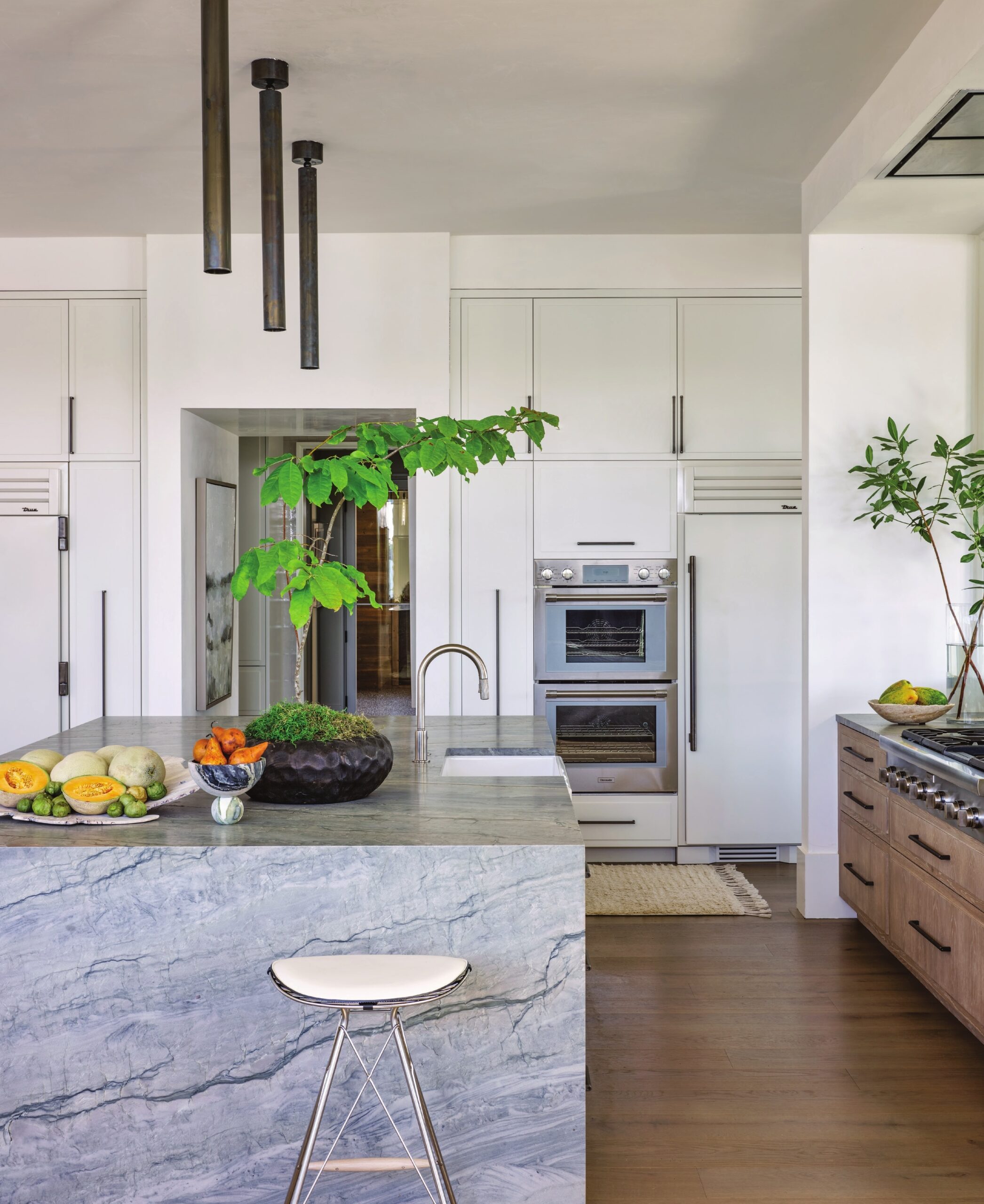 Clad in Brazilian quartzite, the kitchen island lends a sleek, modern profile, complemented by black pendants from R Hughes.