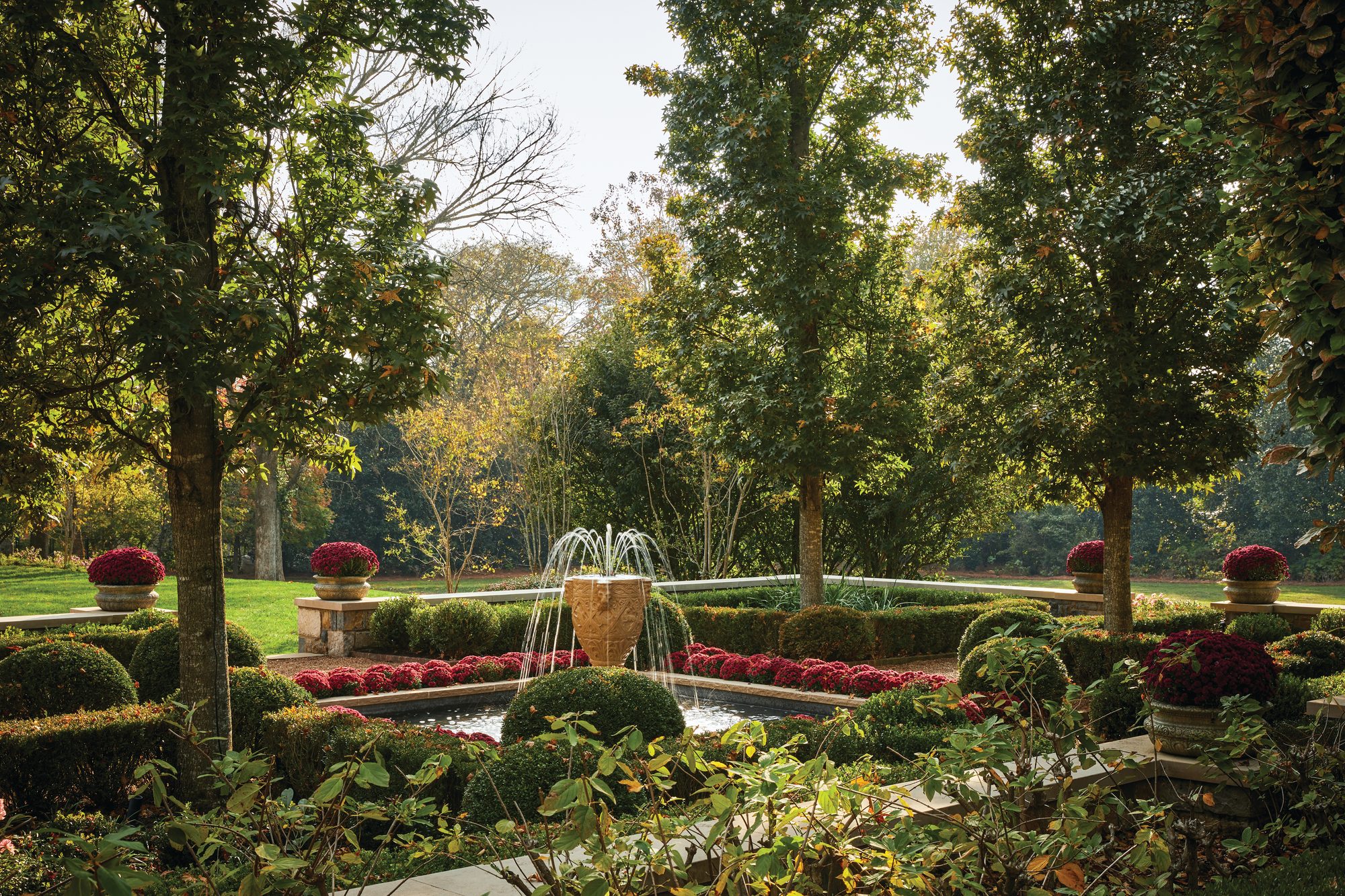 Formal garden with a stone fountain, clipped hedges, and mature trees forming an axis behind the Nashville estate