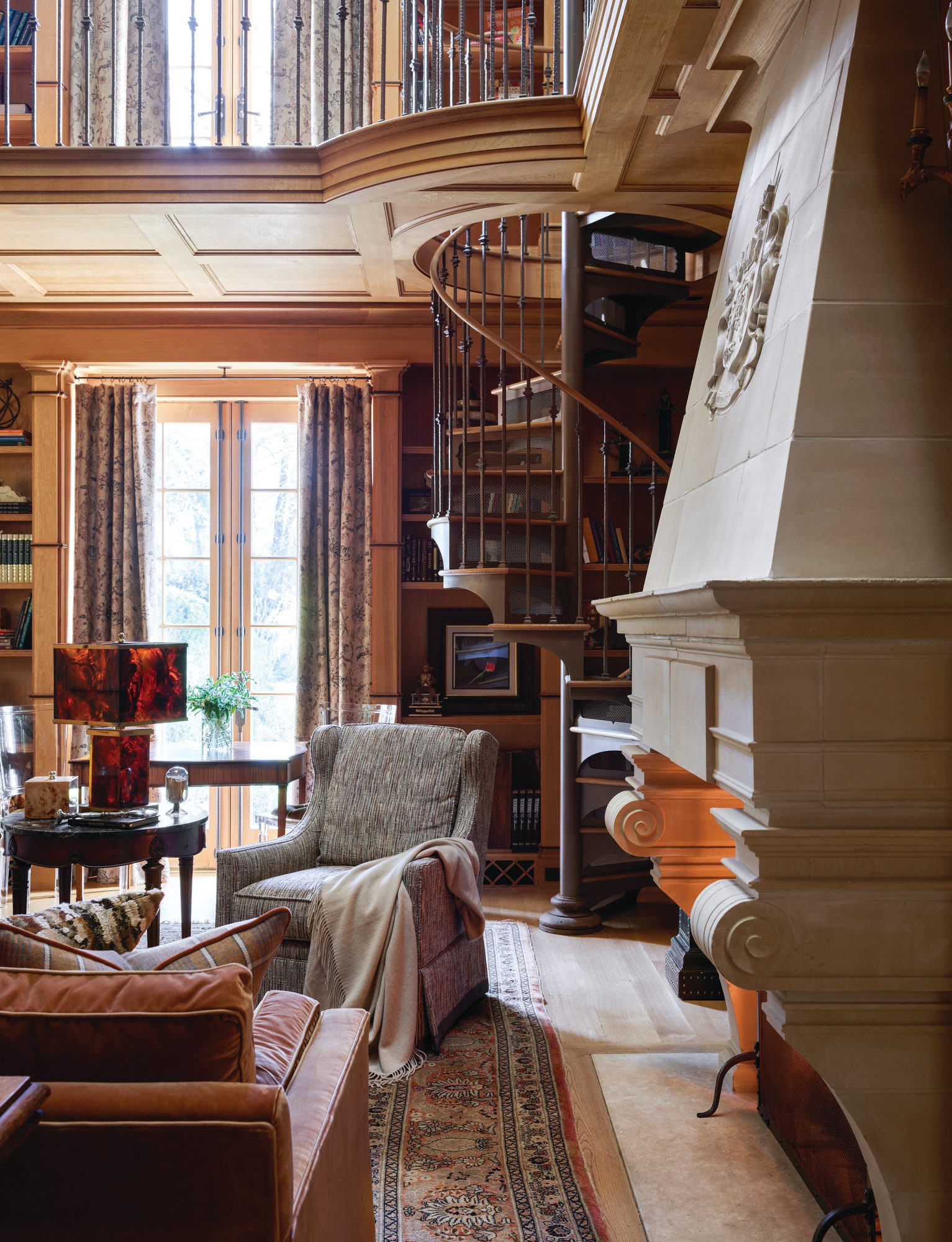 Wood-paneled library with an original limestone fireplace and a corner spiral staircase leading to the second level