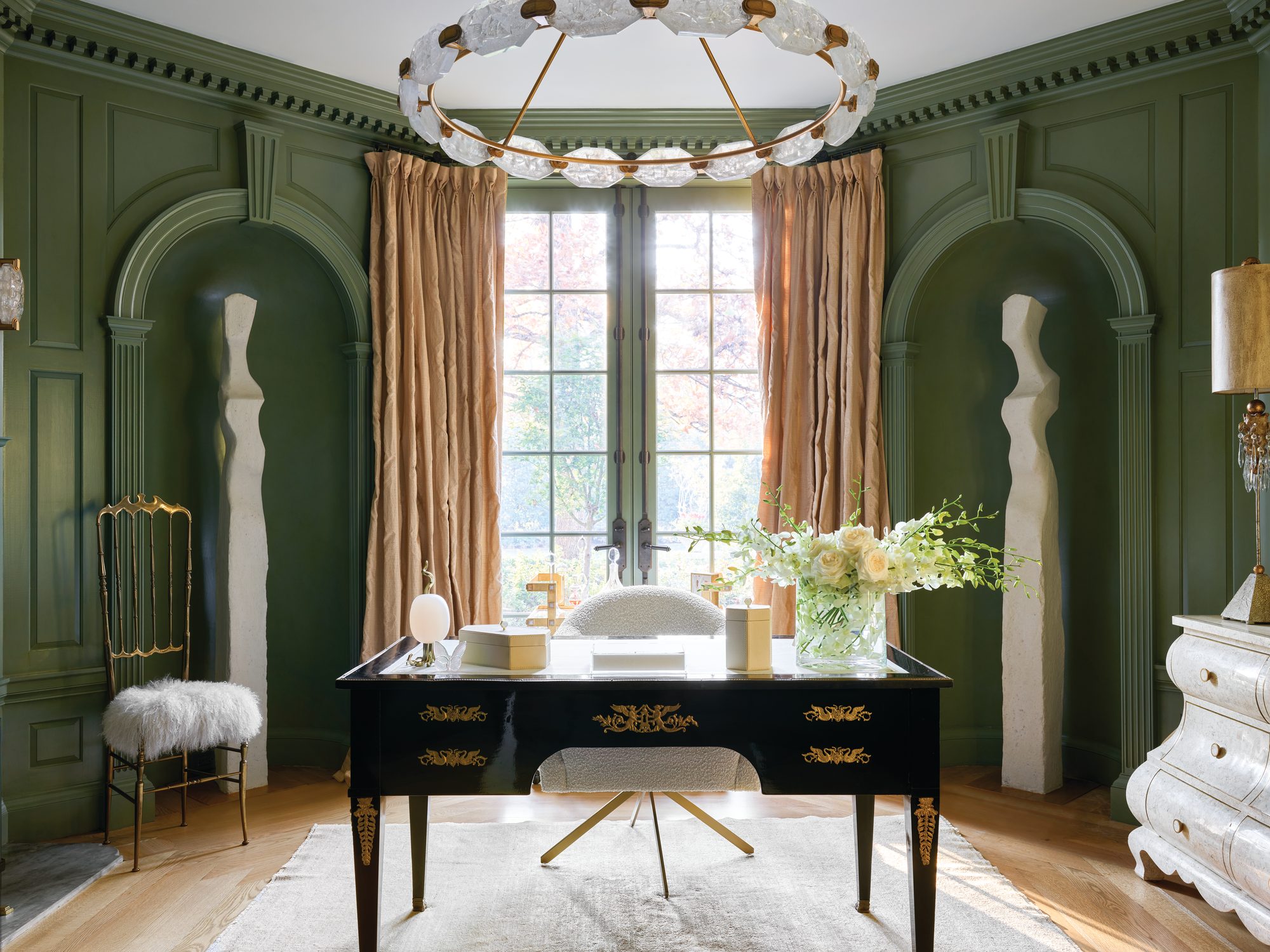 Green-paneled office with arched niches, a black-and-gilt desk, and a circular chandelier beneath a coved ceiling