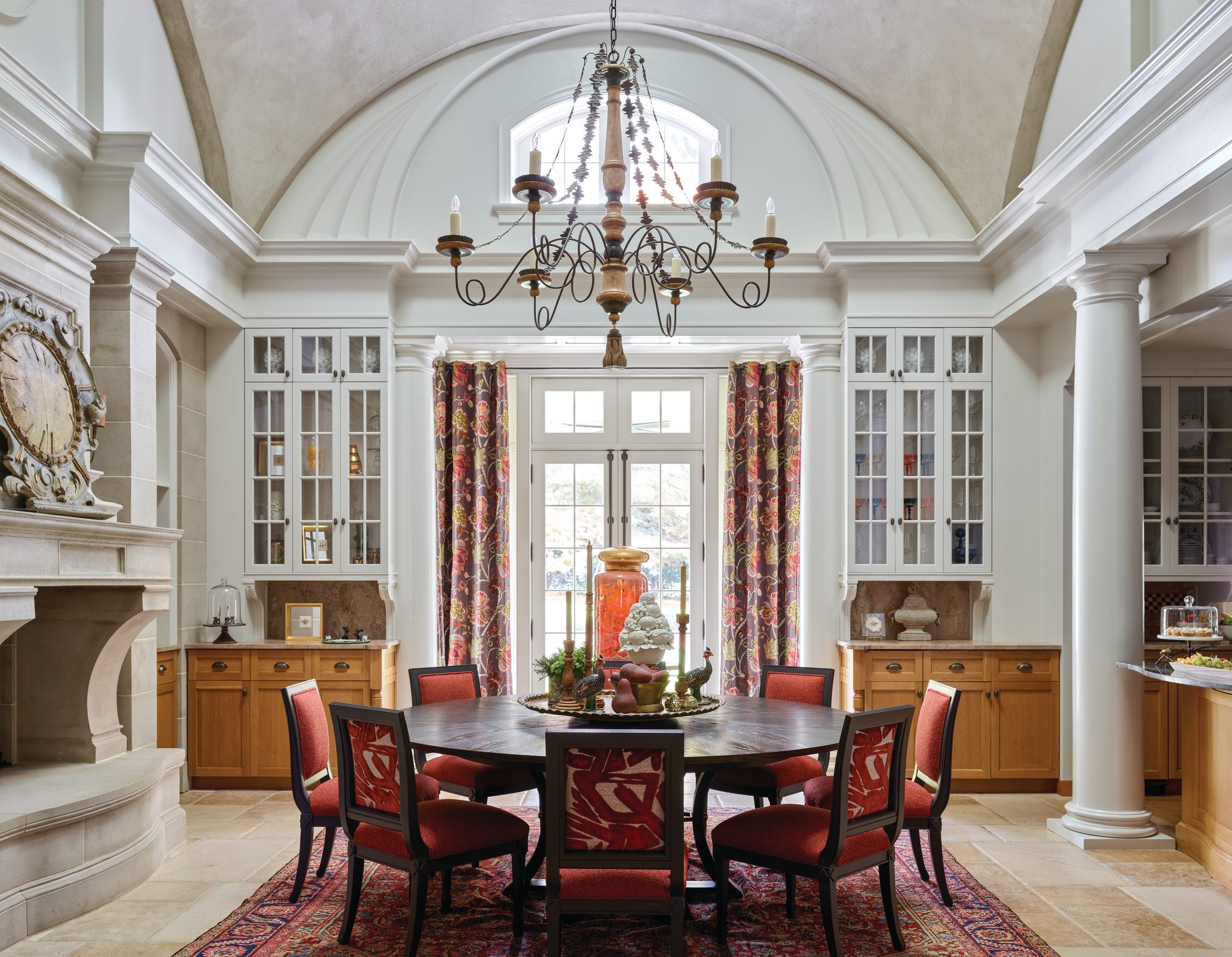 Breakfast room with a barrel-vaulted ceiling, limestone fireplace, glass-front cabinetry, and an eight-person round table with red chairs