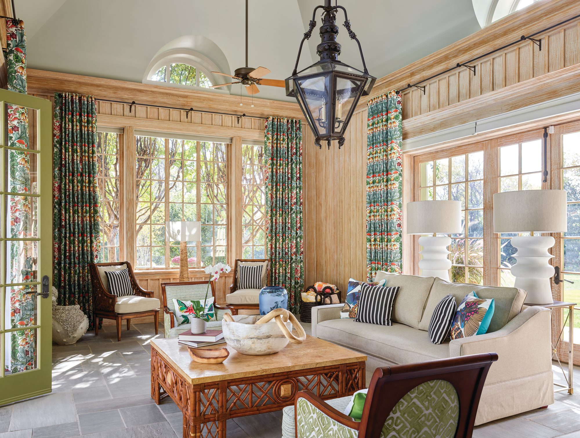 Pool house interior with cerused wood paneling, a vaulted ceiling, a large lantern, floral draperies, and bamboo furnishings