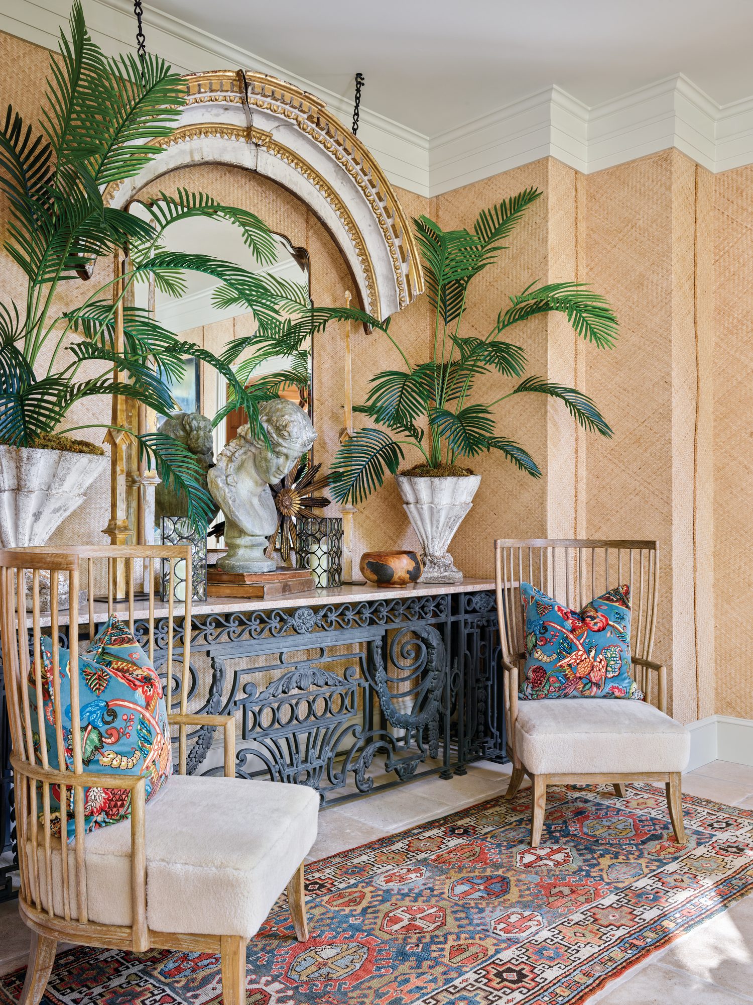 Sunroom foyer with tropical mural wallpaper, an arched niche, potted palms, and a pair of white chairs on a floral rug