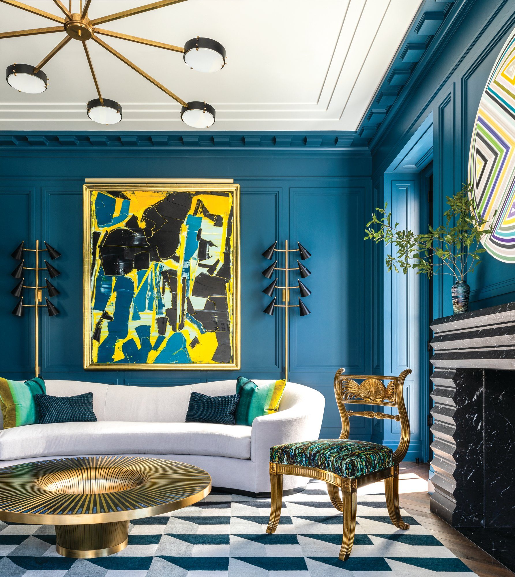 Living room with blue paneled walls, a curved white sofa, a black marble fireplace, geometric stone floors, and a bold yellow-and-blue abstract painting