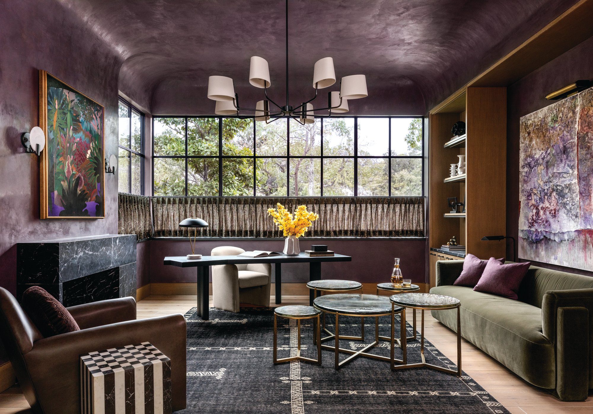 Sitting room with plum plaster walls, a marble fireplace, an olive velvet sofa, and black-framed windows overlooking greenery
