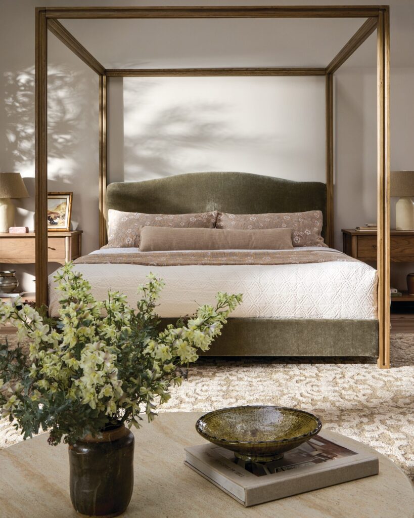 Bedroom by Amber Lewis with a bronze canopy bed, olive upholstered headboard, and flowering branches