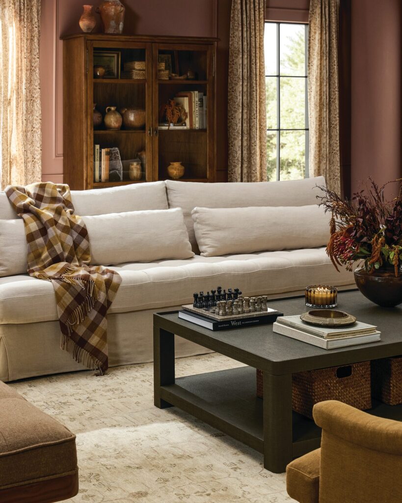 Living room by Amber Lewis with a linen sofa, plaid throw, dark wood coffee table, and vintage rug