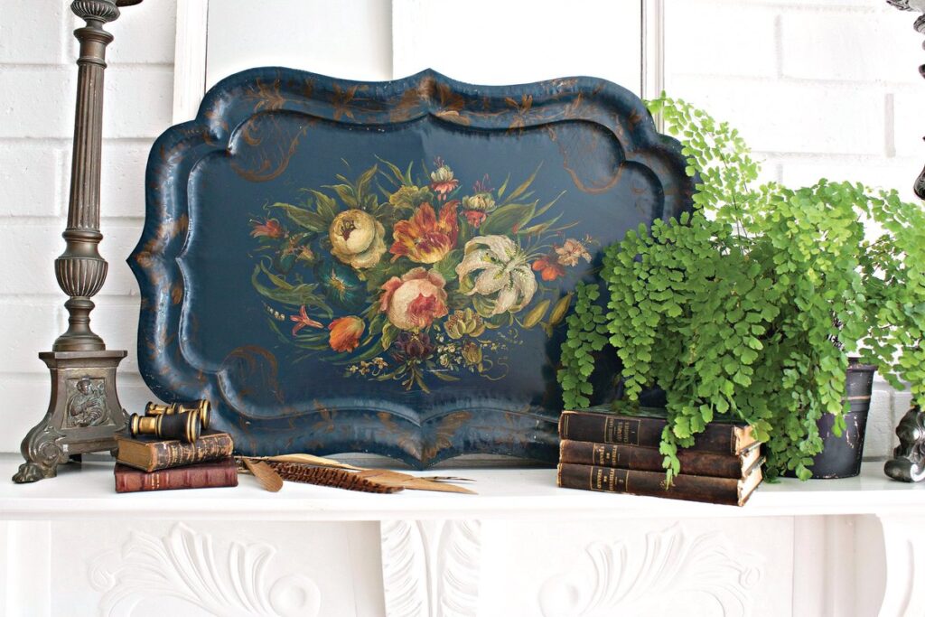 Antique blue tole tray hand-painted with a floral bouquet, displayed on a white mantel beside ferns