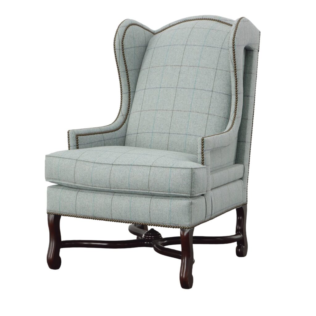 High-back wing chair in seafoam windowpane plaid with nailhead trim on carved dark legs with a stretcher base