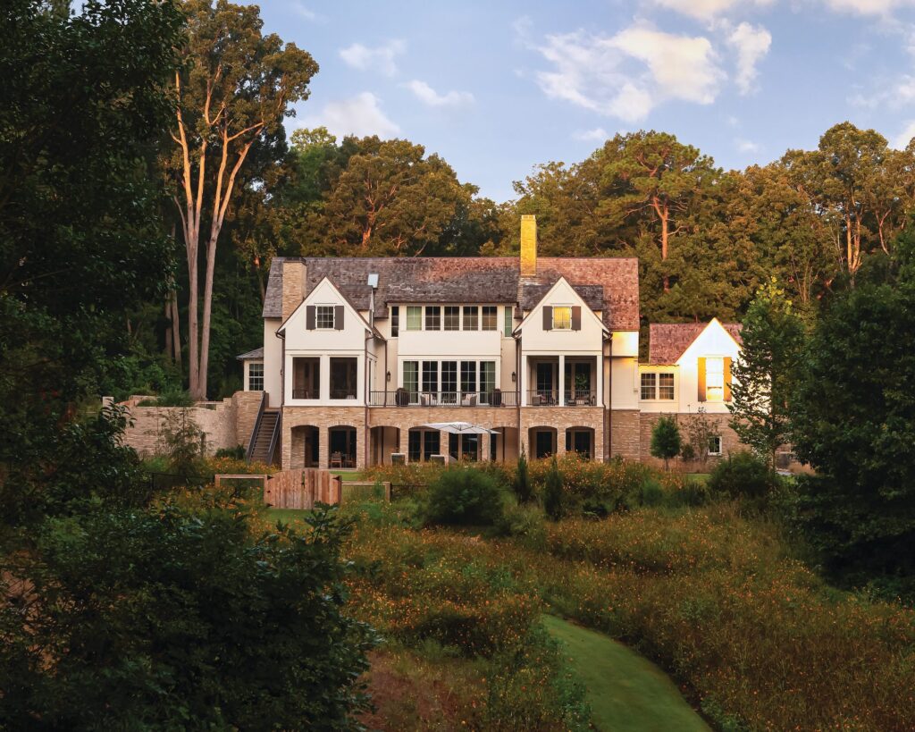 Symmetrical back of the country house with stone archways and terrace, surrounded by woods and fields of wildflowers and grasses