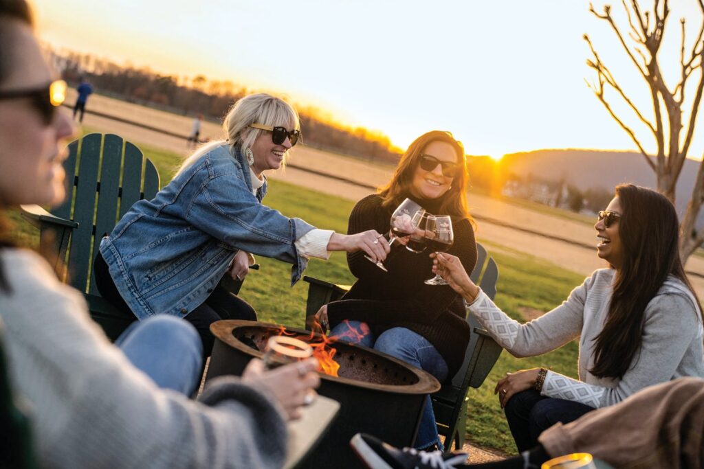 Friends toasting with wine around a fire pit on the lawn of a Charlottesville-area vineyard at sunset