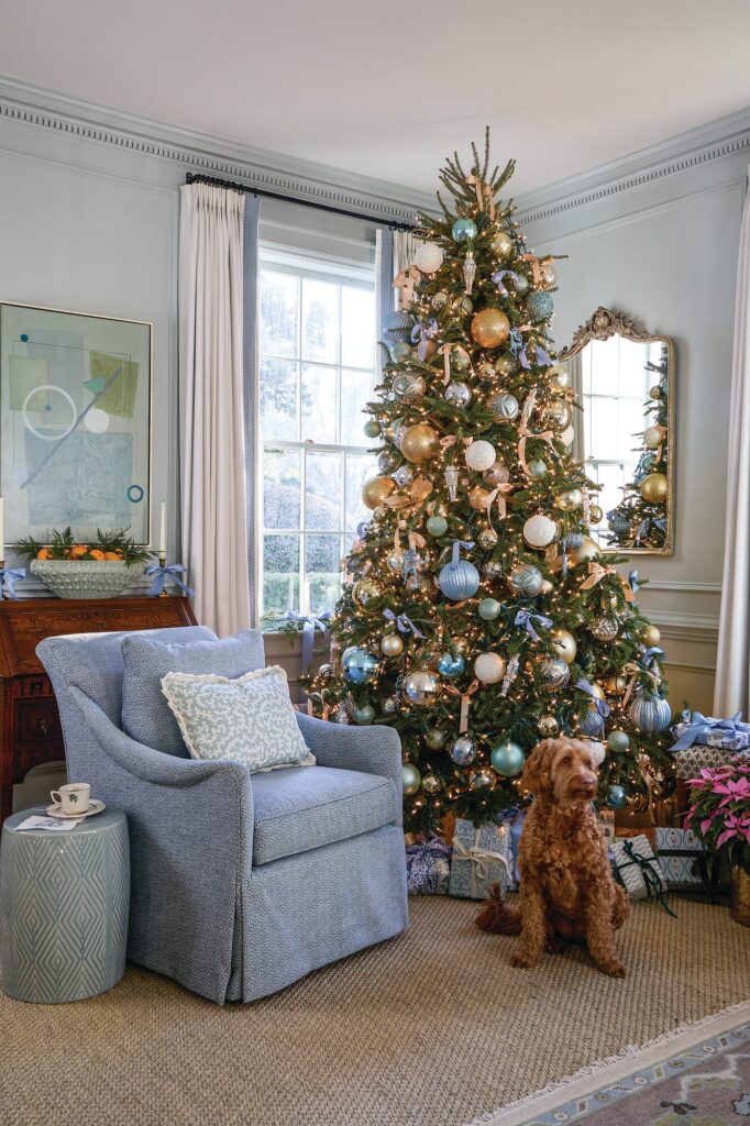 Living room Christmas tree trimmed in frosty blue, champagne, silver, and ivory baubles beside a blue armchair and the family dog