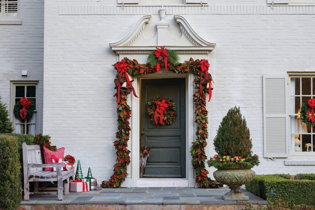 White-painted brick Federal-style home in Montgomery, Alabama, with a front door framed in magnolia garland, red bows, and a wreath