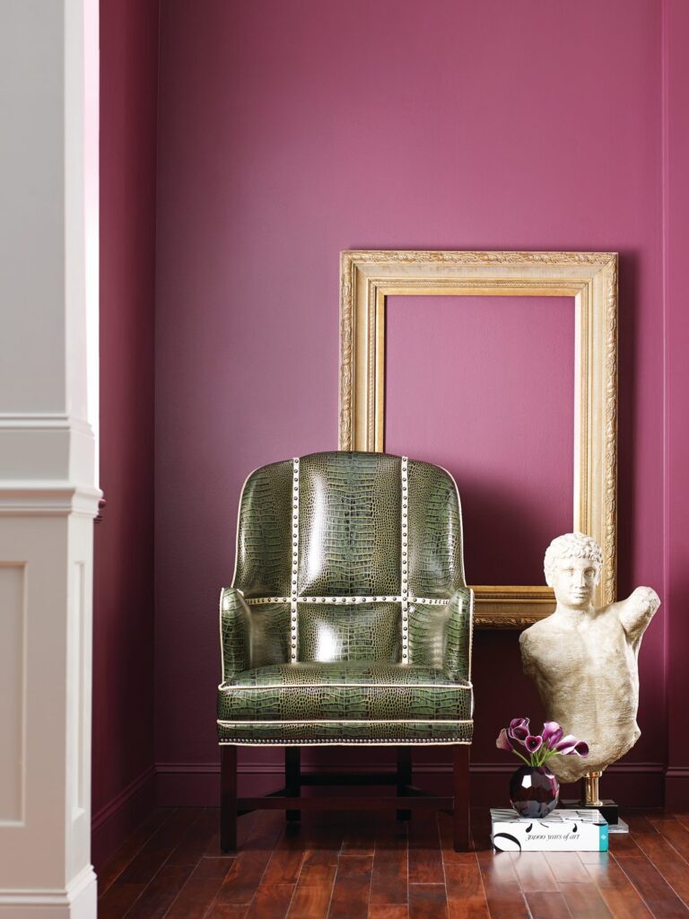 Faulkner wing chair in moss green leather with nailhead trim against a magenta wall beside a gilt frame and a marble bust