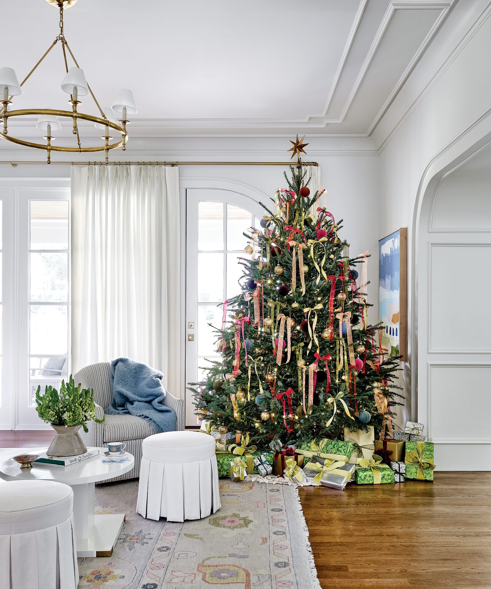 Family room Christmas tree adorned with varying shades of ribbons and ornaments beside skirted ottomans