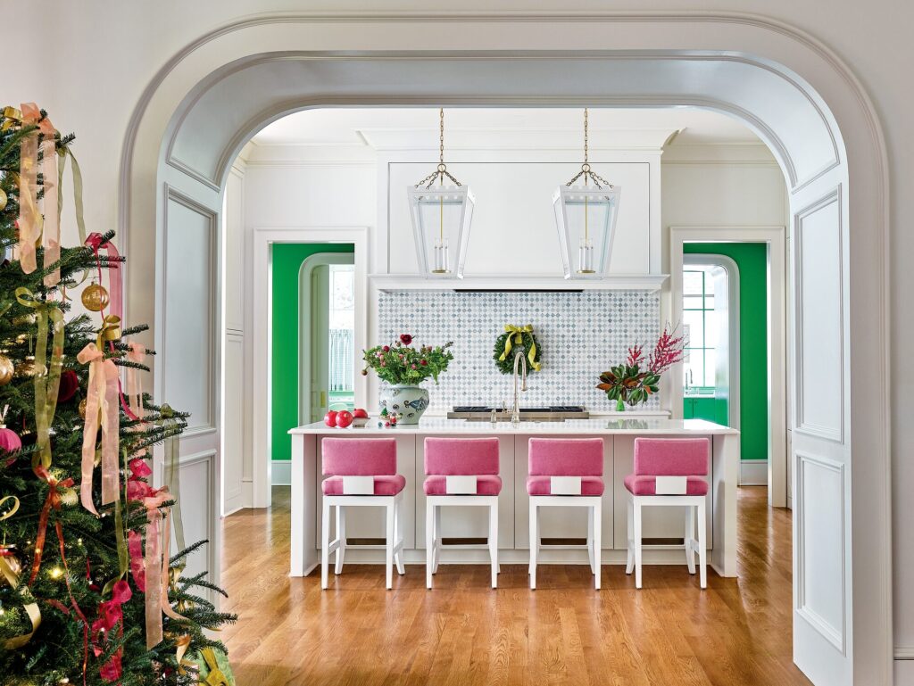 Archway-framed white kitchen with pink barstools, a blue-and-white vase of red ranunculus, and an evergreen wreath over the stove