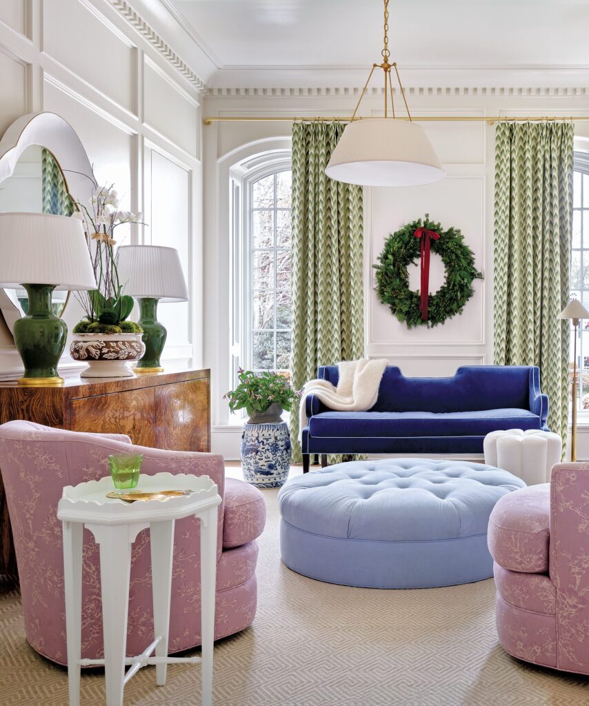 Study with a deep blue sofa, a wreath with red ribbon, pink swivel chairs, and a round upholstered ottoman