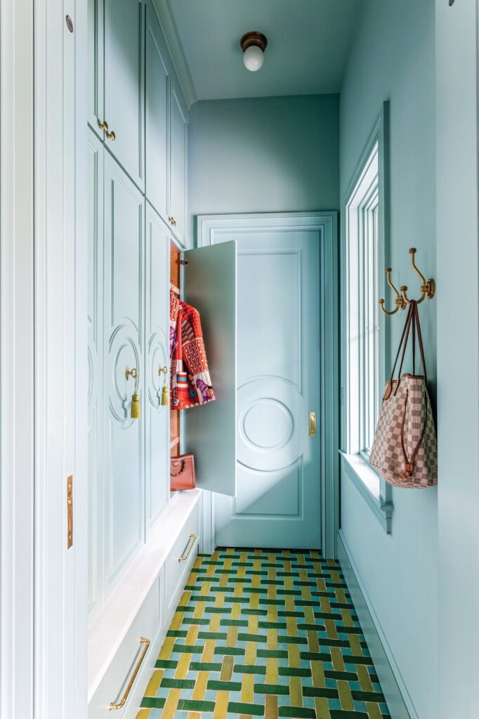 Aqua blue mudroom with built-in cabinets, brass coat hooks, and a green and yellow patterned Popham tile floor