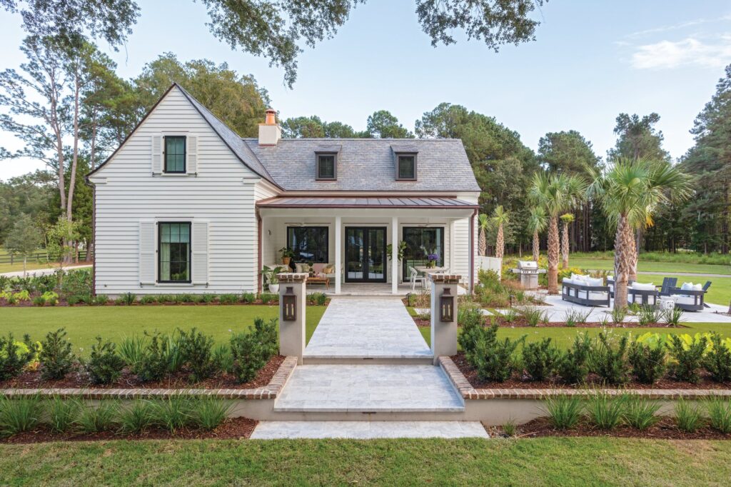 White Lowcountry cottage with a salvaged slate roof, dormers, a front walk lined with boxwoods, and palmettos