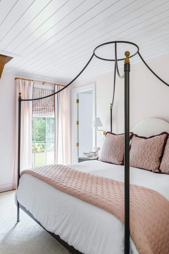 Primary bedroom with a black iron canopy bed, a blush quilt and patterned pillows, and soft pink walls