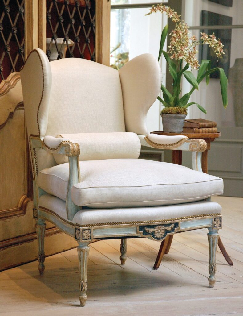 Guinevere armchair with an ivory cushion and bolster on a carved, painted French-style frame beside an orchid