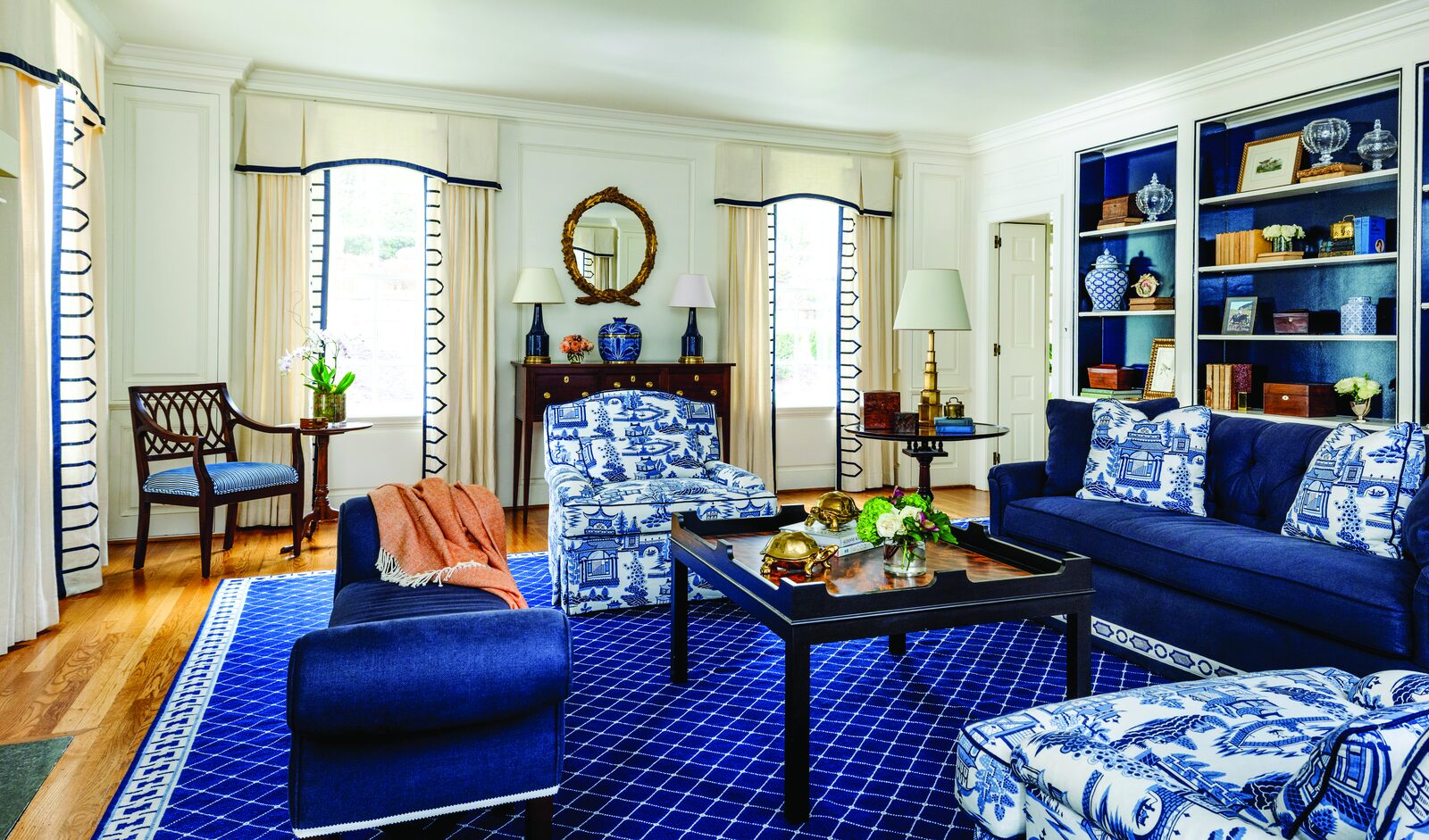 Living room with a navy sofa, blue-and-white patterned chaises, a navy lattice rug, and bookshelves lined in blue