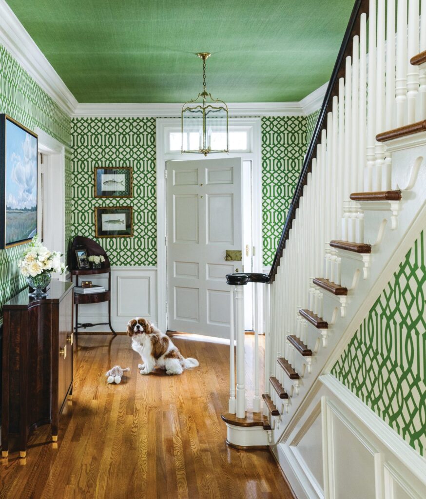 Entry hall with green trellis wallpaper, a green ceiling, a white staircase, and a King Charles spaniel on the wood floor
