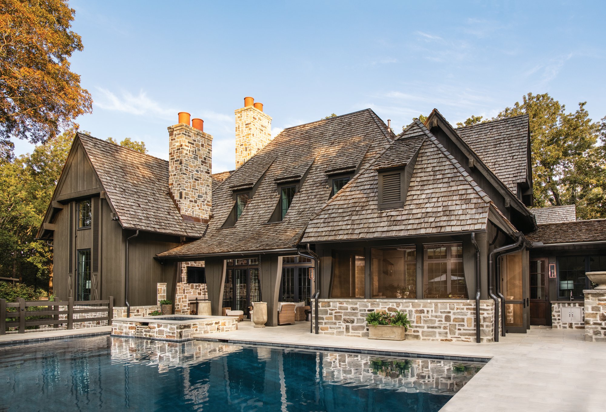 Back exterior of an Alabama home with a pool and spa, stone chimneys, a screened porch, and a cedar shake roof