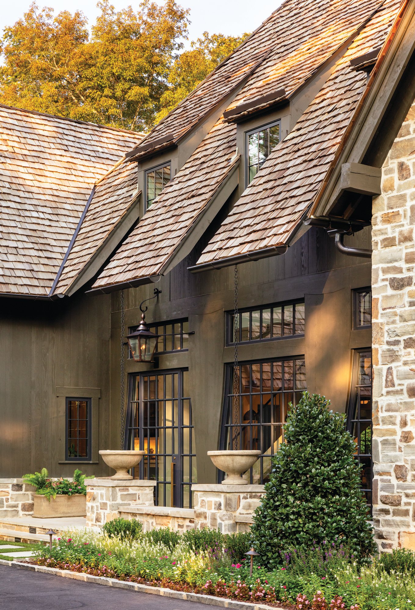 Entry of an Alabama home with steel-framed glass doors, cast stone urns, a hanging lantern, and rain chains beneath a cedar shake roof