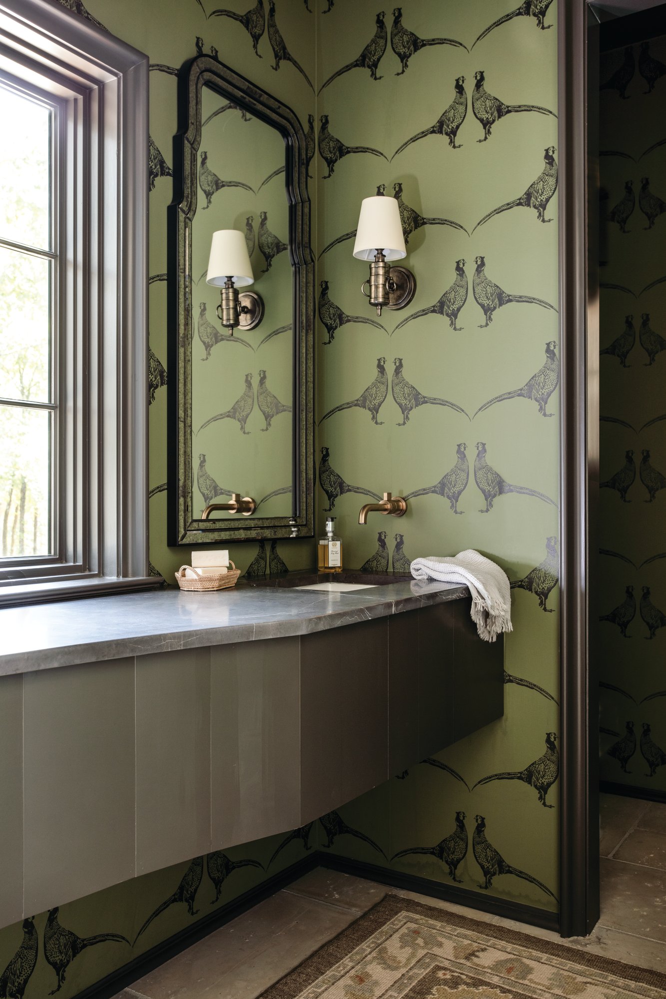 Powder bath with green pheasant wallpaper, an off-center undermount sink, an aged brass wall-mount faucet, and an antiqued mirror