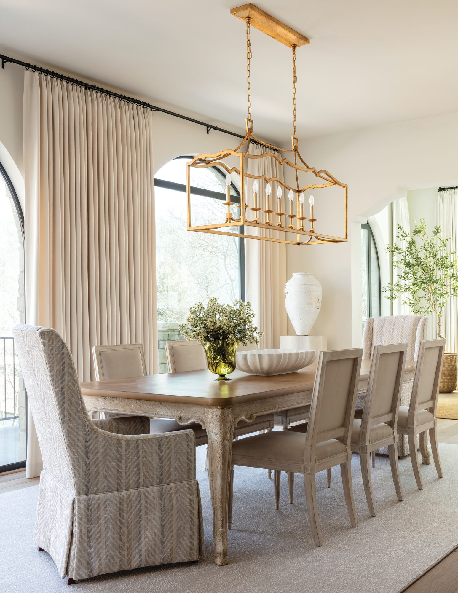 Dining room with a refinished light-wood table, slipcovered upholstered chairs, and a brass linear lantern beneath an arched window