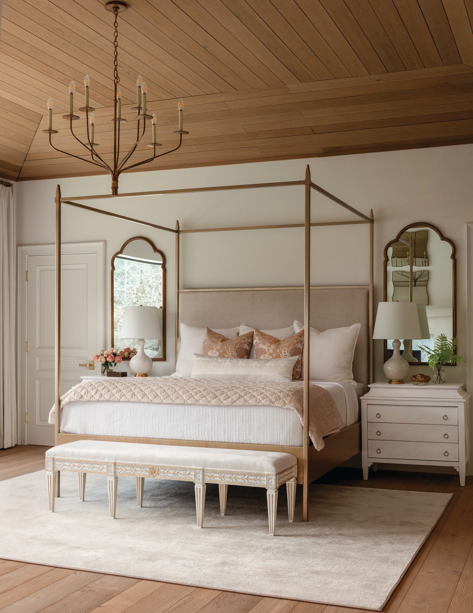 Primary bedroom with a wood-plank ceiling, a four-poster bed dressed in pink-and-white bedding, and an upholstered bench on wood floors