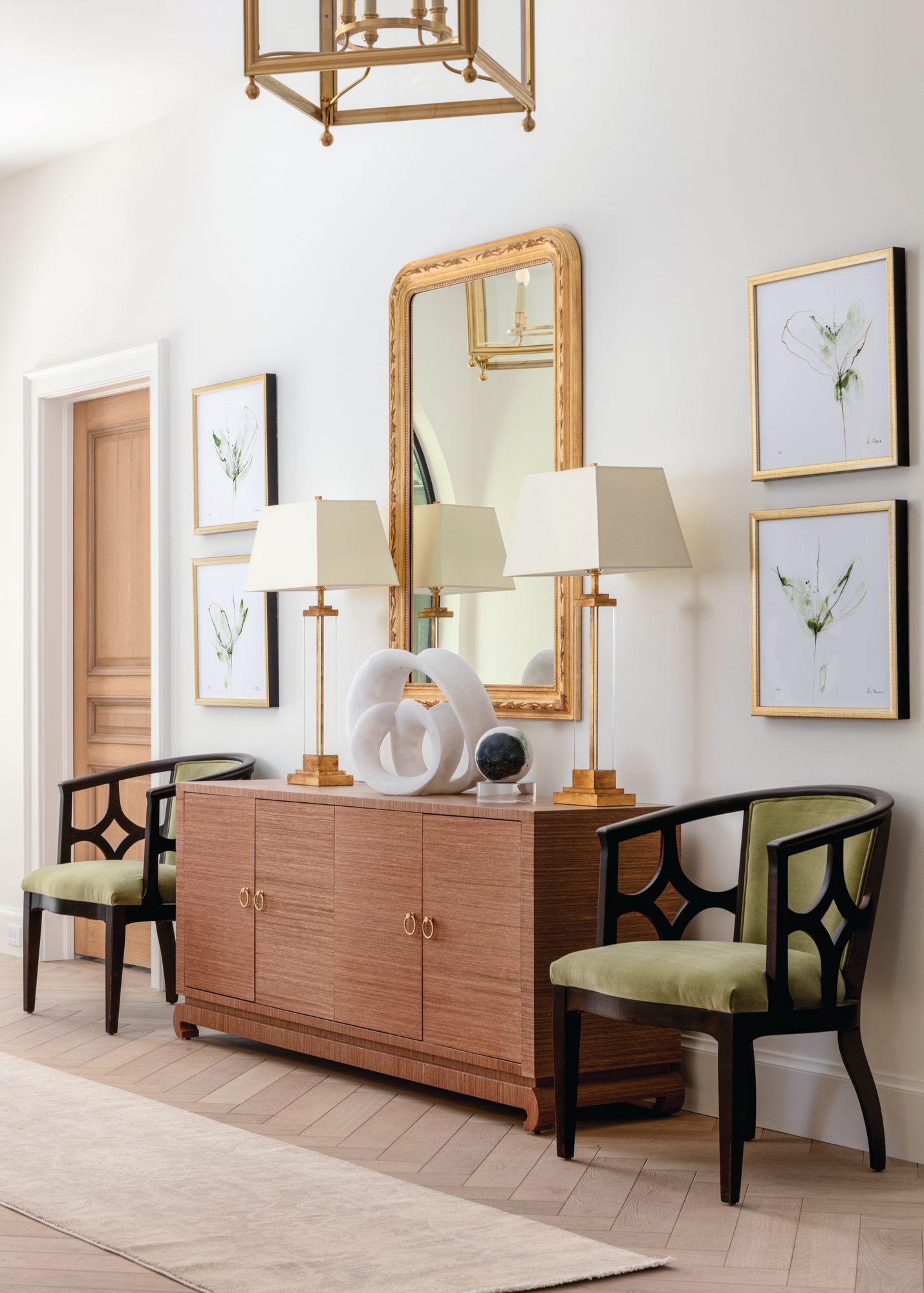 Entry with a pair of green upholstered chairs flanking a textured grasscloth sideboard topped by a gilt mirror and framed botanical artwork