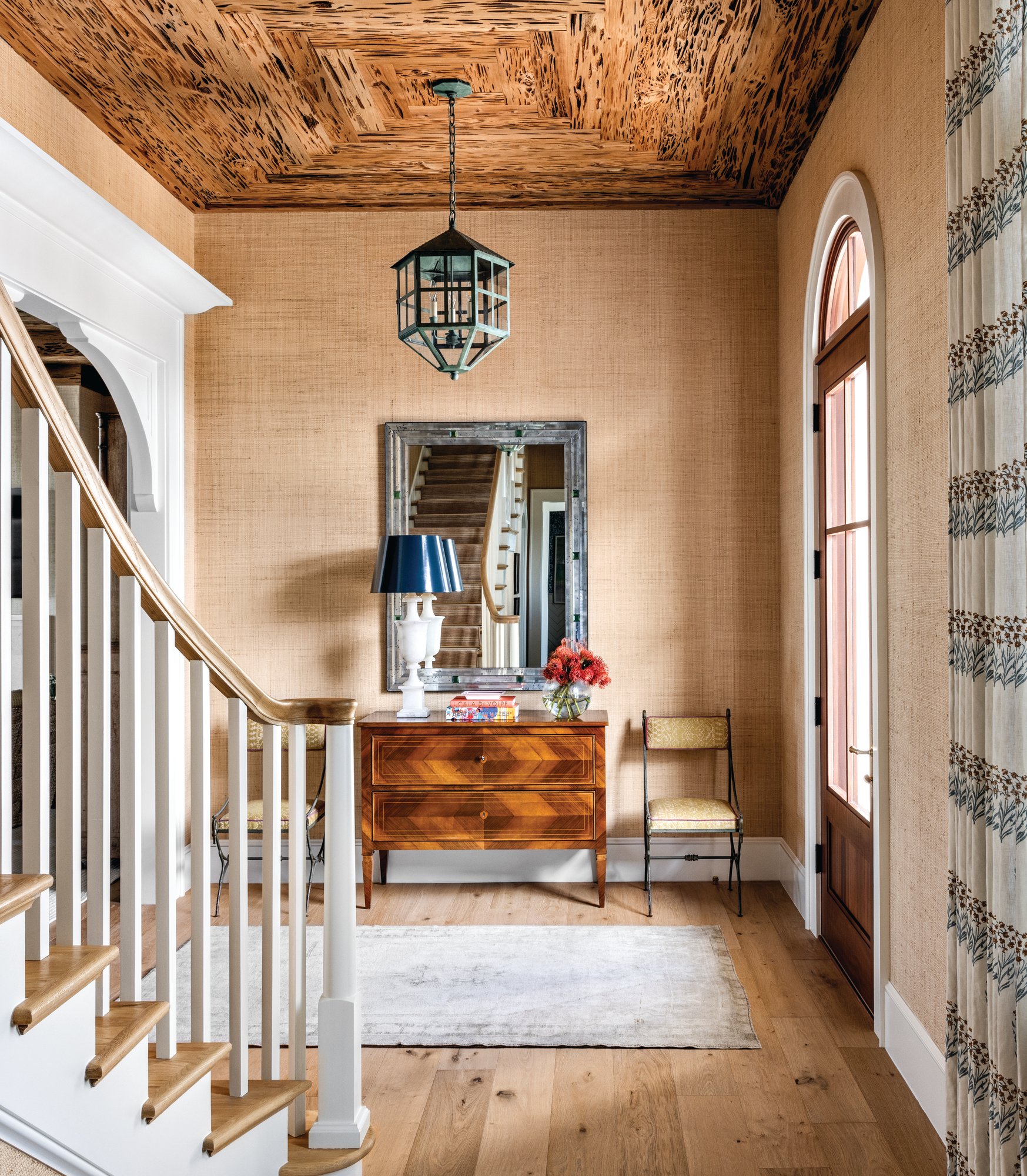 Entry with a pecky cypress ceiling, grasscloth walls, a verdigris lantern, an inlaid wood commode, and an arched wood front door