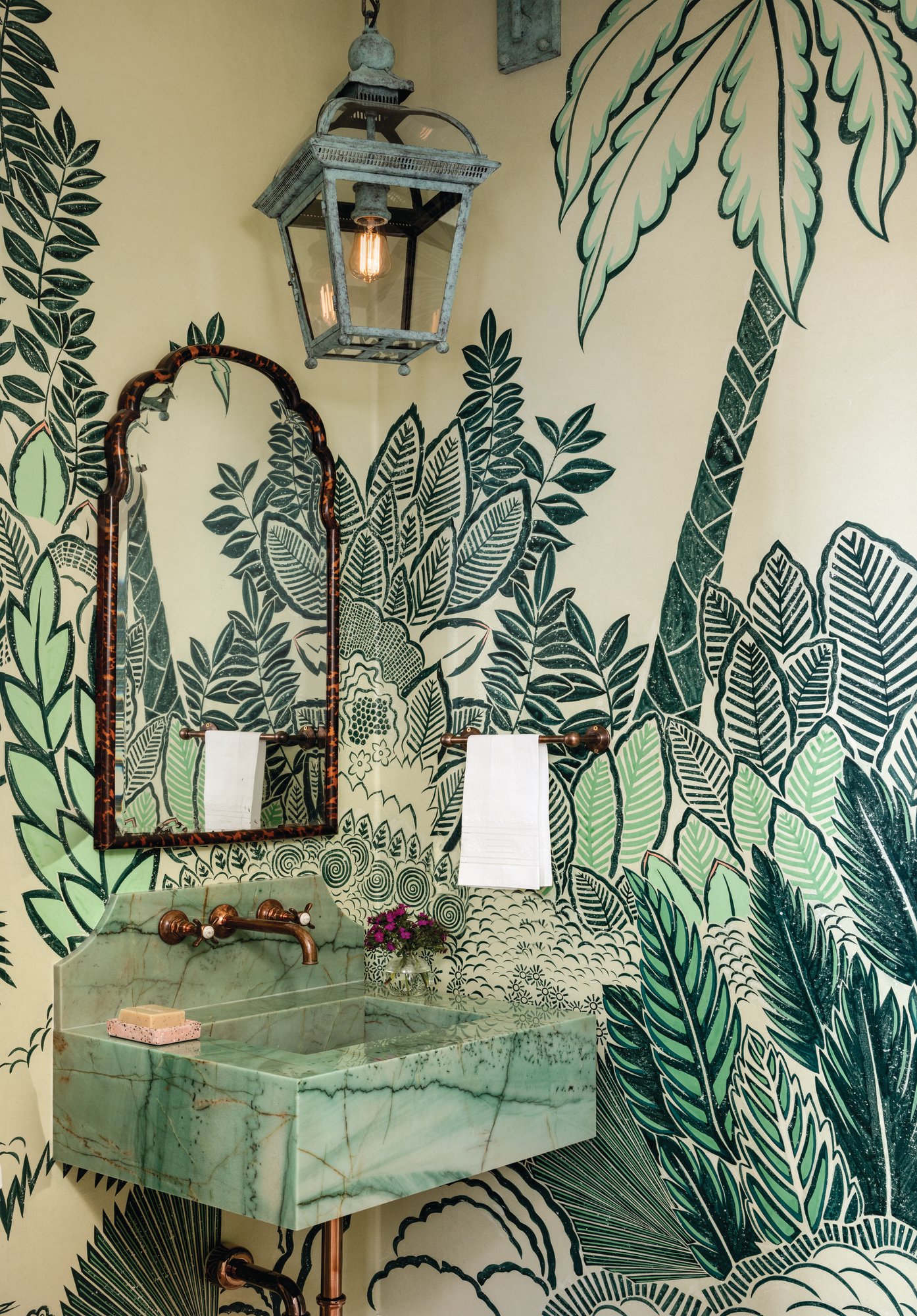 Powder bath wrapped in green de Gournay botanical wallpaper with a green marble sink, aged copper fittings, a tortoiseshell mirror, and a verdigris lantern